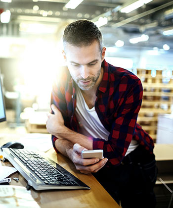 man at his computer looking at a smartphone