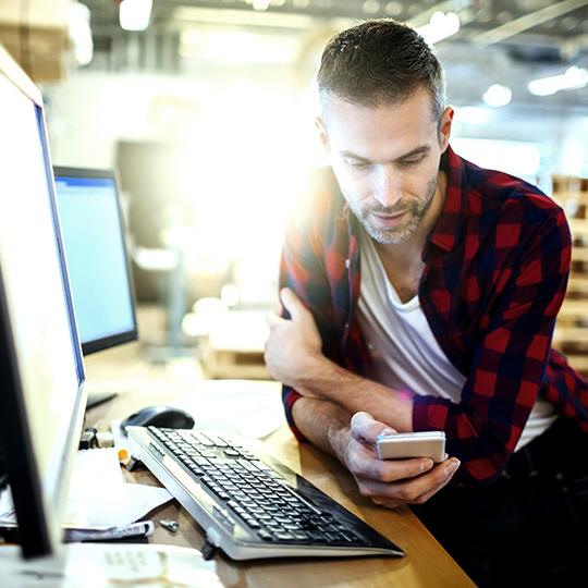 Grow your business towards Digital Transformation man at his computer looking at a smartphone