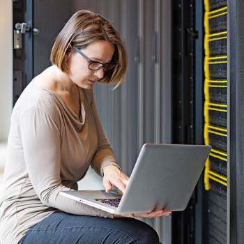 A sua rede está em risco? woman working on a laptop in a server room